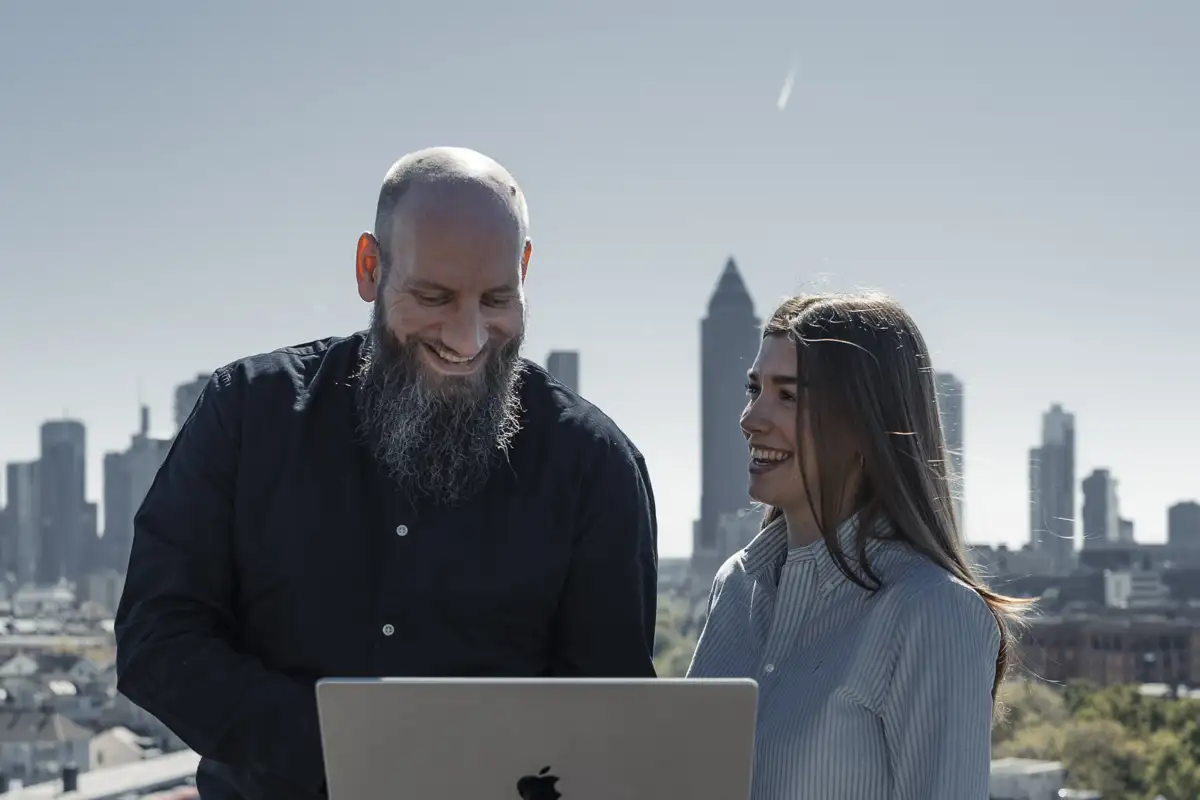 Zwei Kollegen am MacBook auf der Dachterrasse mit Frankfurter Skyline